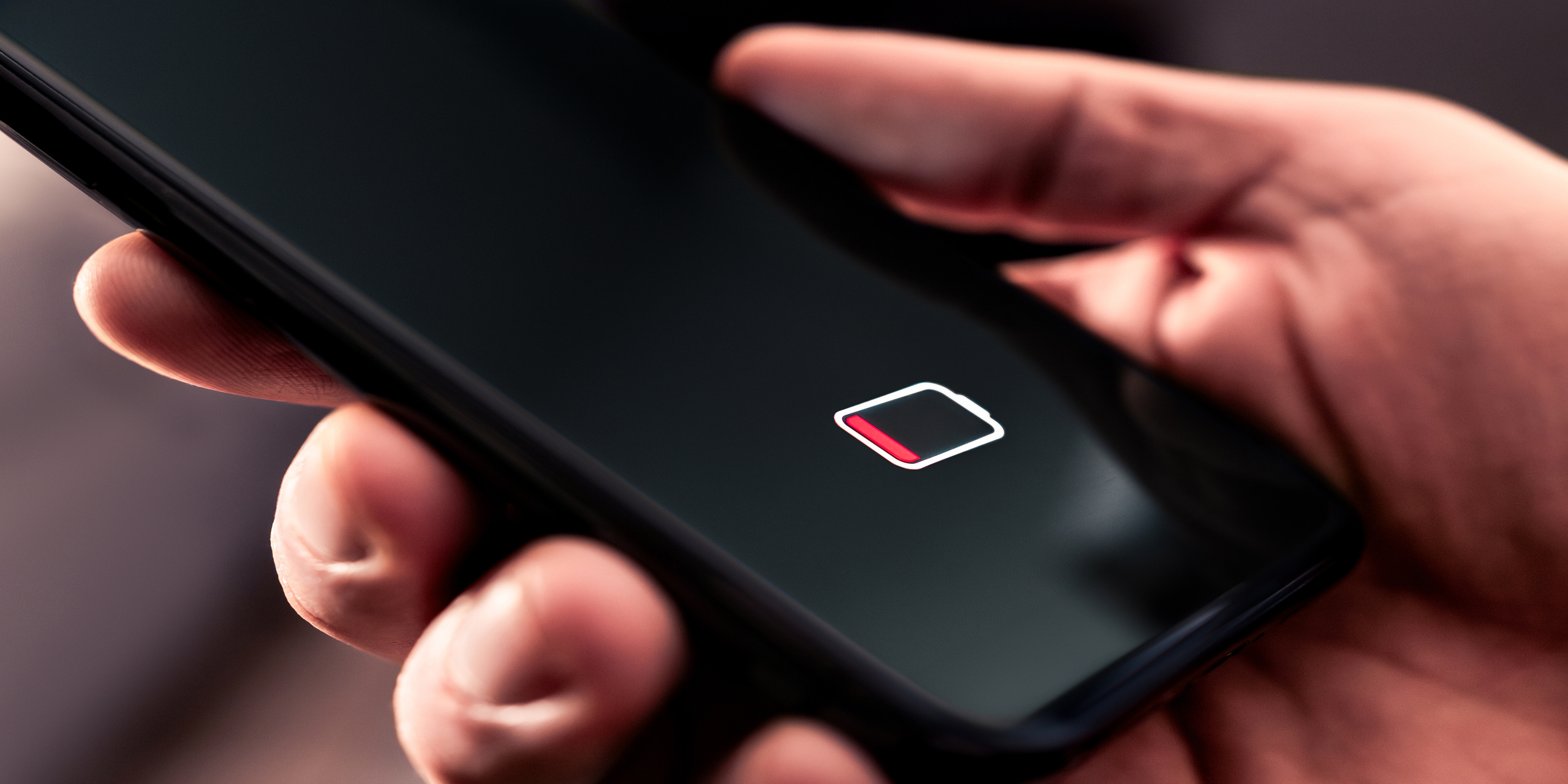 Dłoń trzymająca telefon z widoczną ikonką rozładowanej baterii
