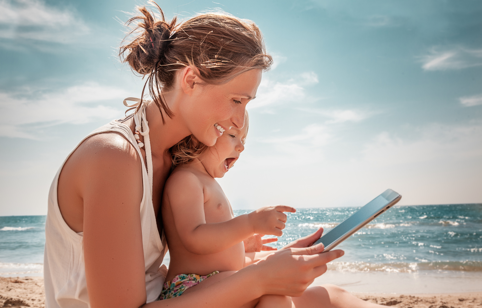 Matka z córką korzystają z internetu na tablecie, siedząc na plaży