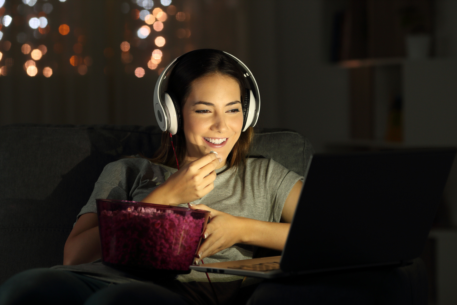 Kobieta w słuchawkach ogląda na laptopie serial na streamingu i je popcorn