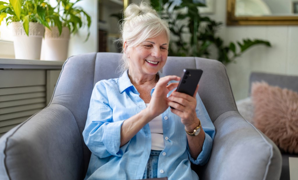Uśmiechnięta seniorka korzysta z internetu na telefonie.