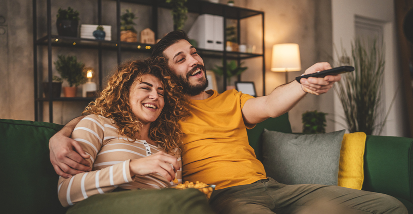 Mężczyzna i kobieta siedzą na kanapie i wybierają, jaki film obejrzeć na platformie streamingowej