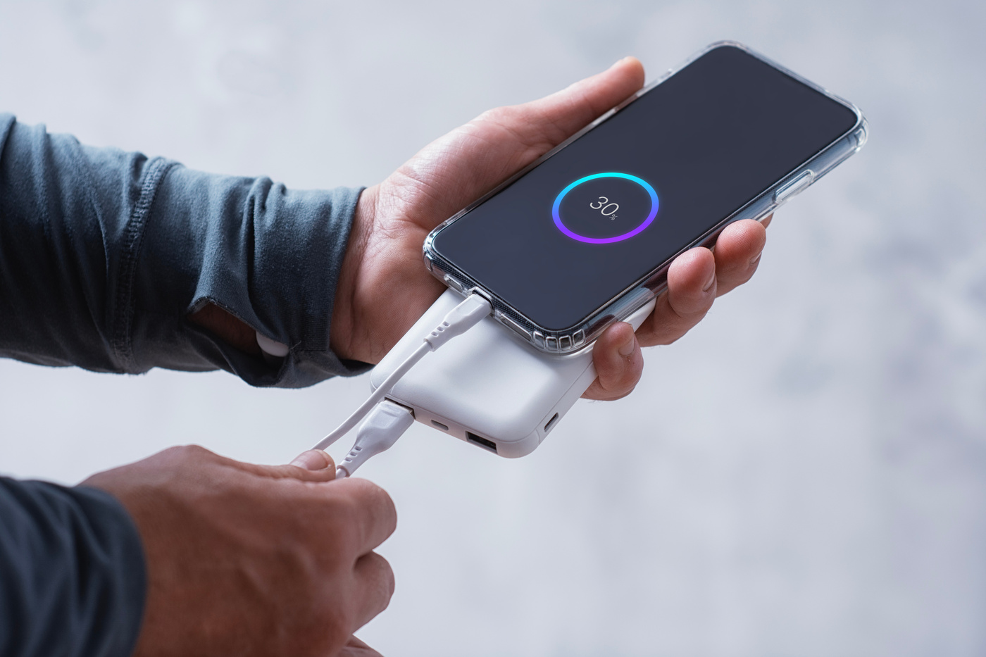 Dłonie trzymają telefon podłączony do powerbanka